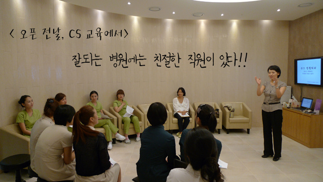 여러명의 여직원과 그들 앞에 서 있는 여 강사를 찍은 사진