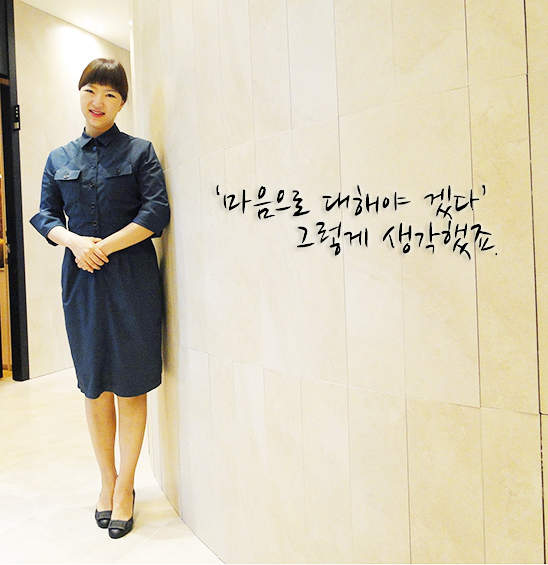 진초록색의 유니폼을 입은 여직원이 두 손을 모으고 미소짓고 있다.