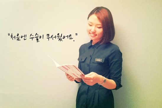 벽에 기대 선 단발머리의 여직원이 소책자를 보며 미소지으며 서 있다.