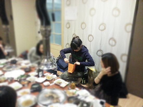 머리를 묶고 남색 후드티를 입은 여자가 선물을 뜯어보는 사진