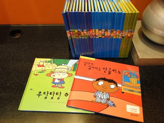 책꼿이에 동화책이 꼿혀있고 두권이 펼쳐져있다. 책제목이 잠자기 싫어하는 안졸리노이다